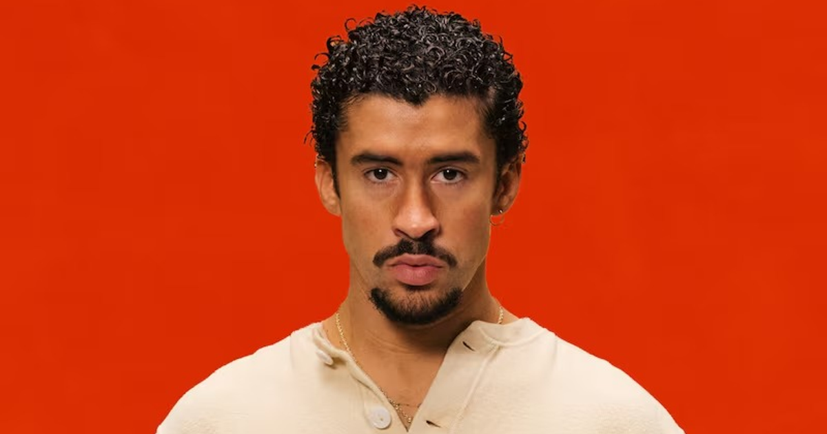 Hombre con cabello rizado y prenda clara sobre fondo rojo, representando a Bad Bunny, máximo artista latino del siglo XXI.