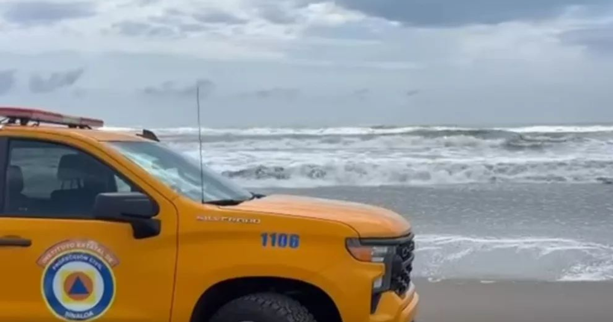 Camión de Protección Civil en playa de Altata con oleaje fuerte y cielo nublado.
