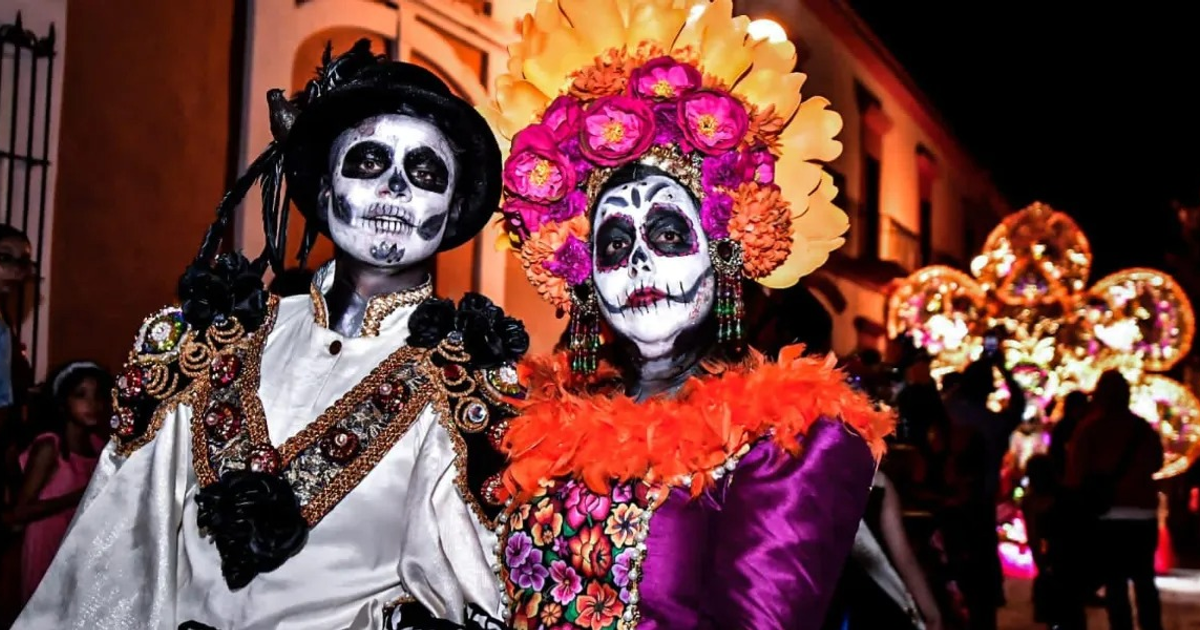 Dos personas con trajes coloridos y maquillaje de calaveras celebran el Día de Muertos en México.