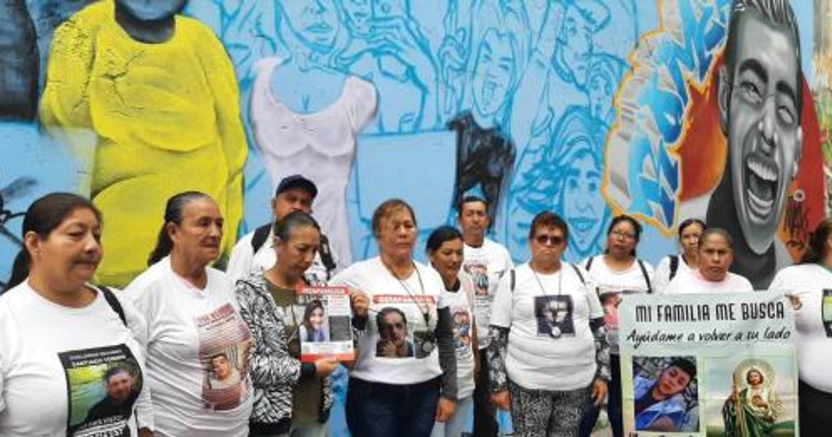 Grupo de mujeres en Jalisco con camisetas de desaparecidos y carteles de búsqueda, mural colorido al fondo.