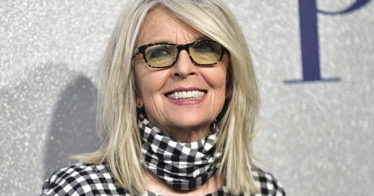 Persona sonriente con cabello rubio y gafas oscuras, vestida a rayas en blanco y negro