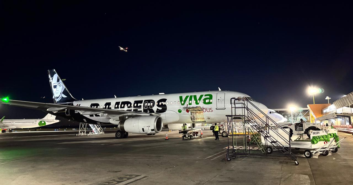 Avión de VivaAerobus en aeropuerto nocturno con personal y equipos de carga