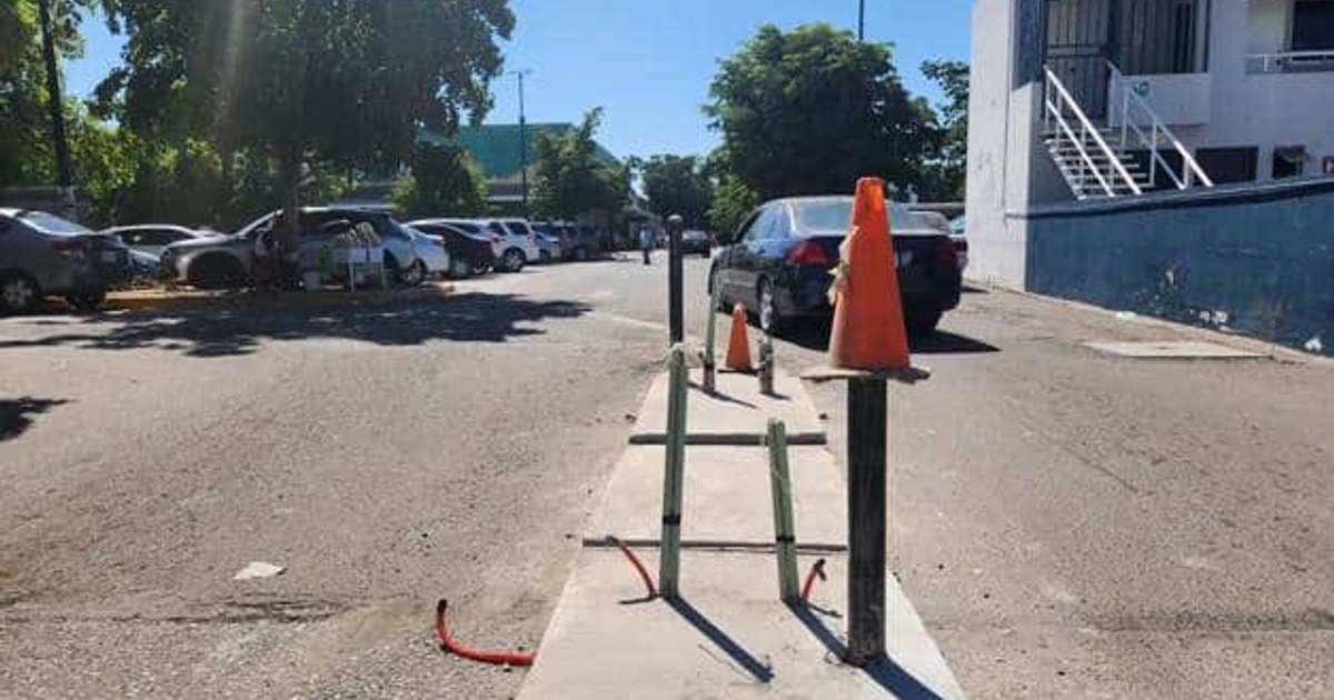 Calle en Los Mochis con vehículos aparcados y conos naranjas, instalación de plumas en Bodega Aurrera.