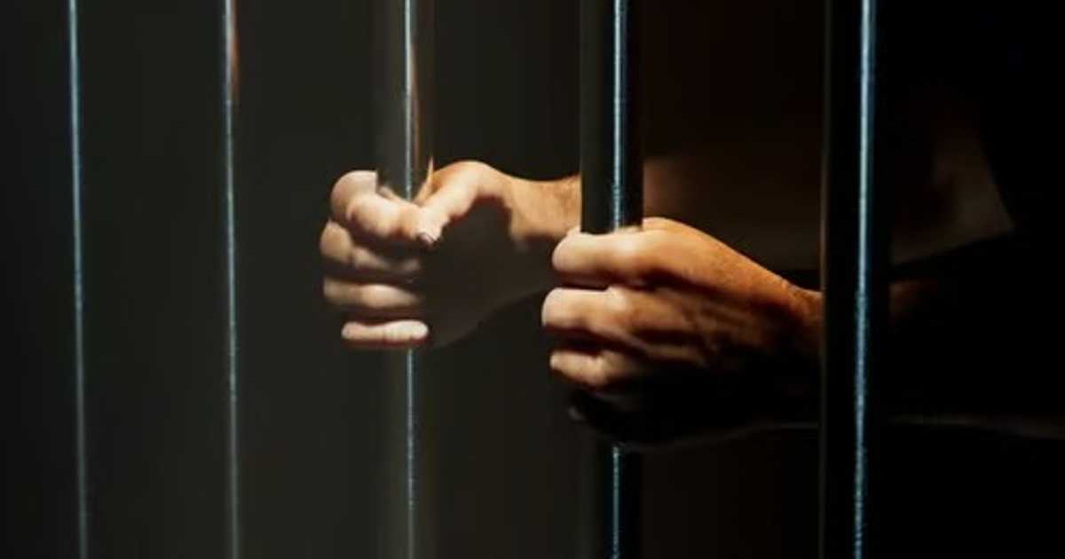 Manos sujetando barras metálicas en un entorno oscuro, simbolizando encarcelamiento.