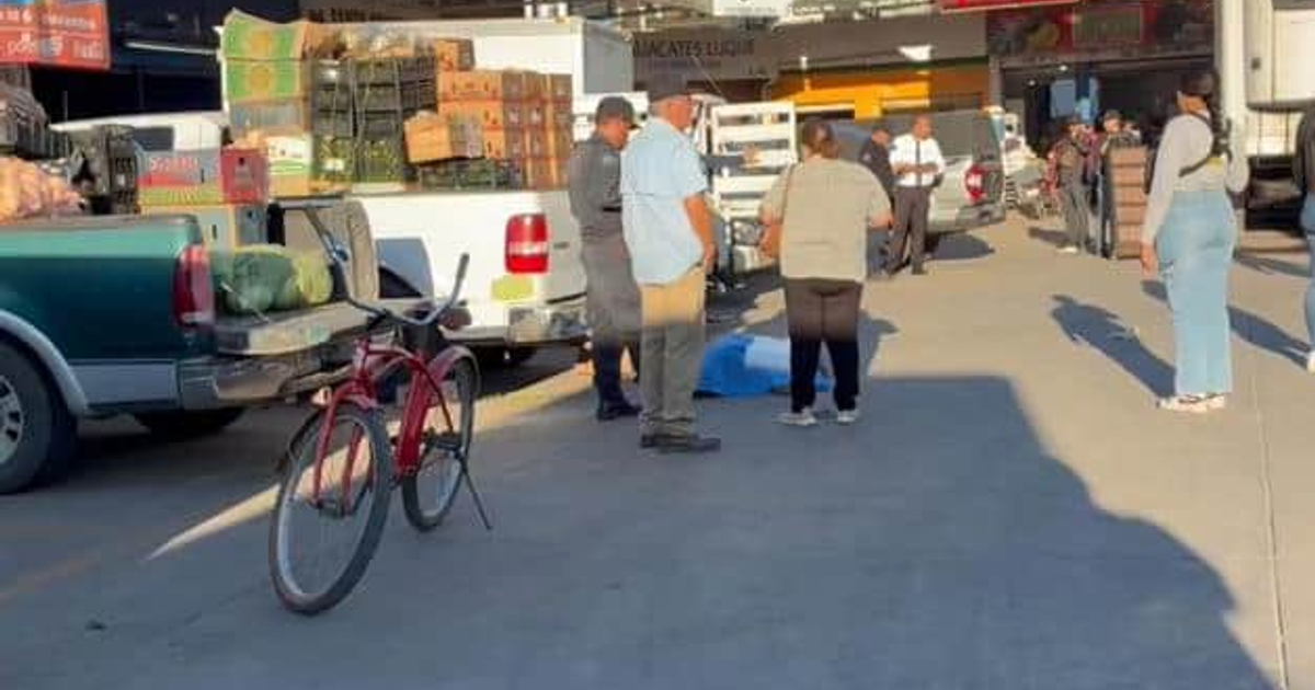 Personas reunidas en un mercado de Los Mochis tras un incidente, con vehículos y una bicicleta roja en primer plano.