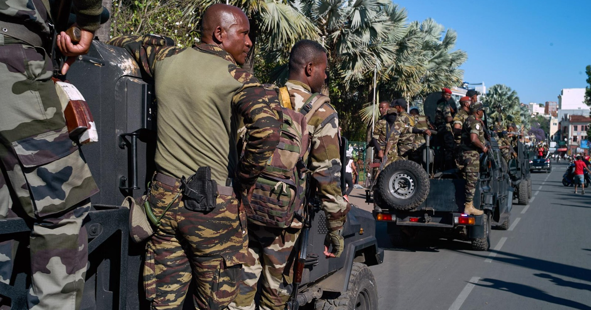 Soldados en uniforme de camuflaje patrullando una calle urbana en Madagascar, con vehículos militares y edificios al fondo.
