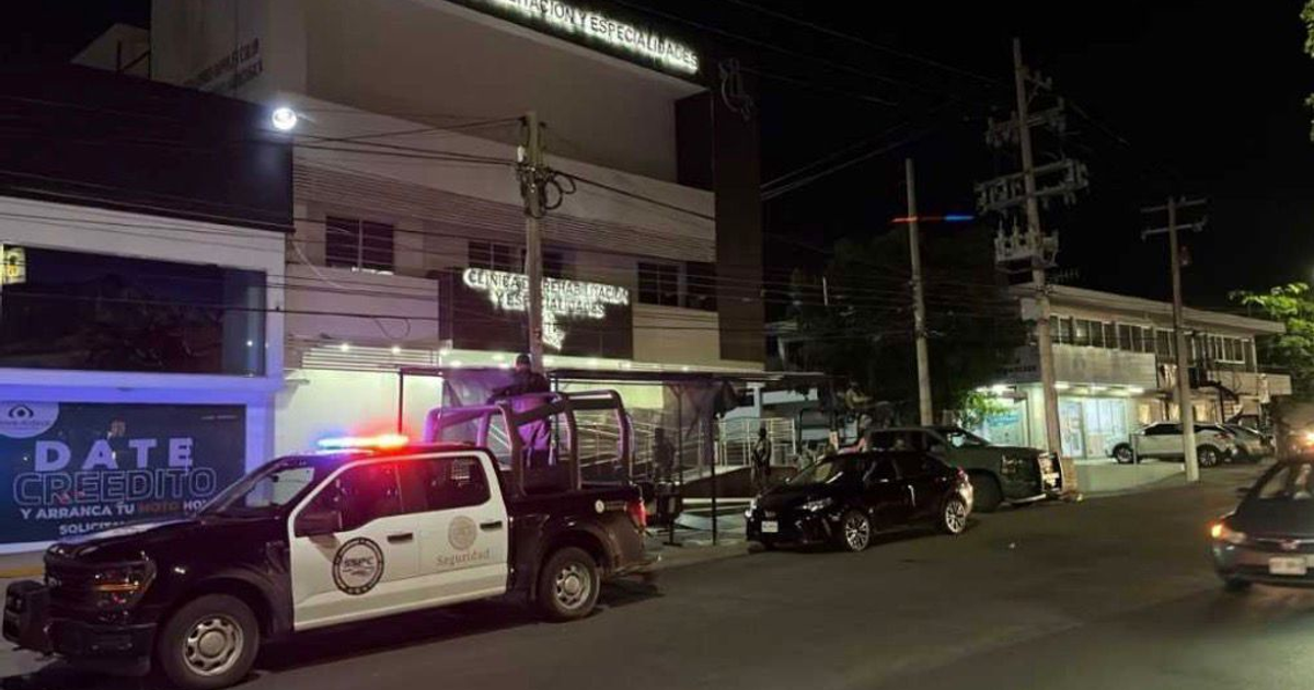 Calle nocturna en Culiacán con vehículo de policía y clínica de fondo