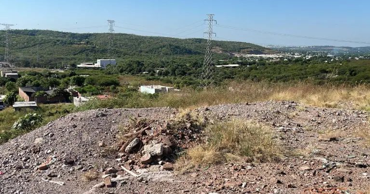 Paisaje rural en Culiacán con escombros, colinas y torres eléctricas bajo un cielo azul.