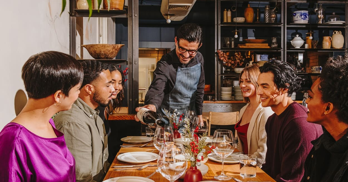 Grupo de personas cenando en un restaurante con camarero sirviendo vino