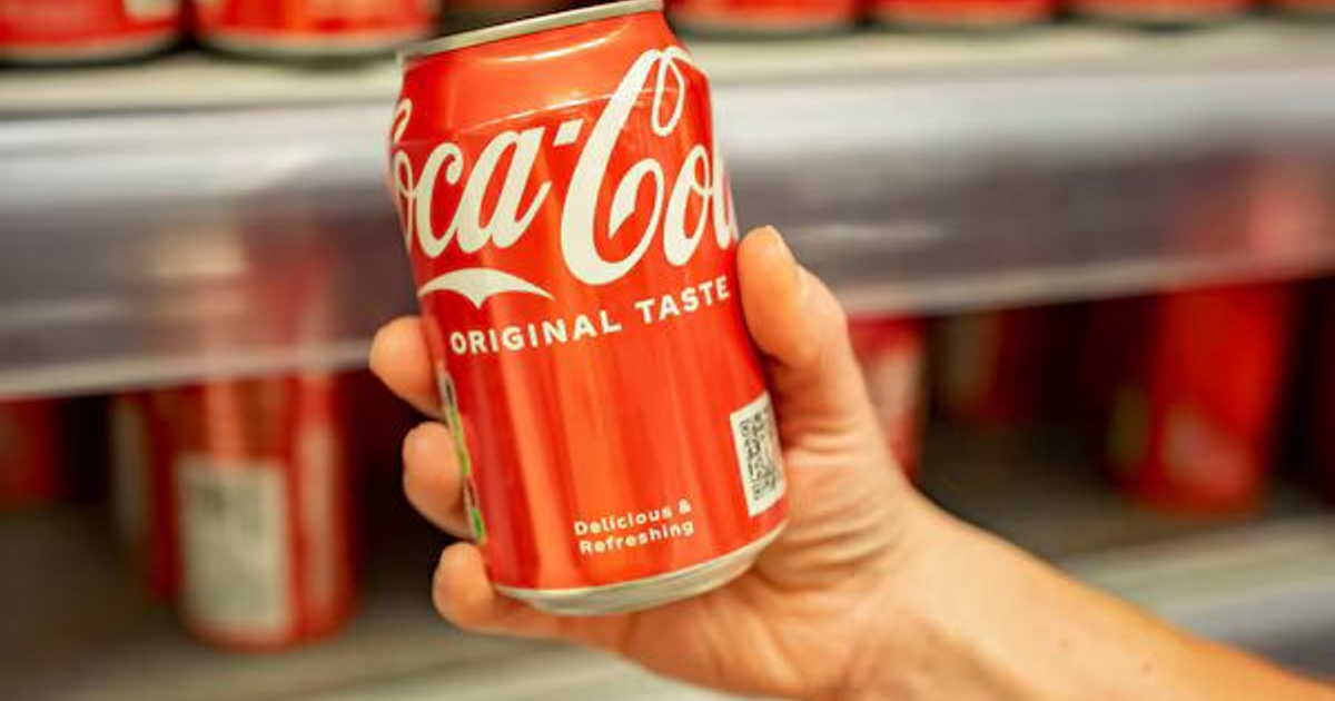 Mano sosteniendo una lata de Coca-Cola en un refrigerador, simbolizando la reducción de calorías en México.