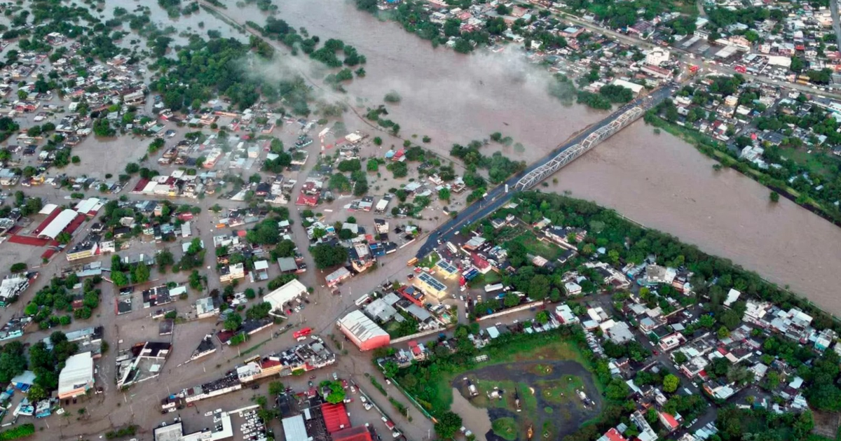 Vista aérea de inundaciones en México con casas y calles sumergidas, y un puente sobre un río desbordado.