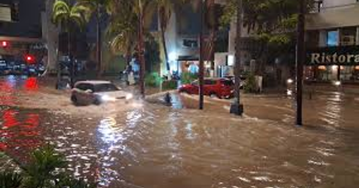 Calle inundada en Mazatlán con vehículos y palmeras durante la noche