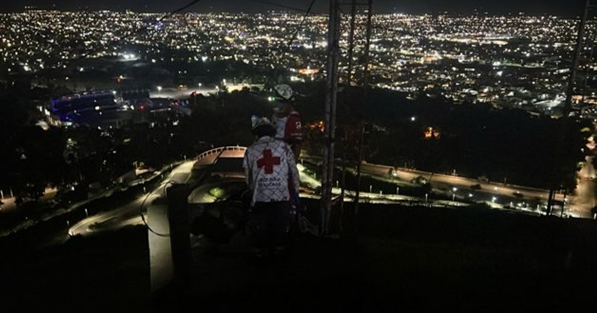 Paramédicos de la Cruz Roja en un rescate nocturno en el Cerro de la Memoria, con la ciudad iluminada al fondo.