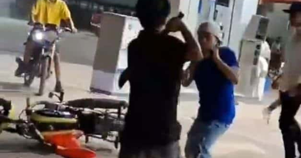 Jóvenes en altercado en gasolinera de San Miguel Zapotitlán, motocicleta caída, tensión en el ambiente.