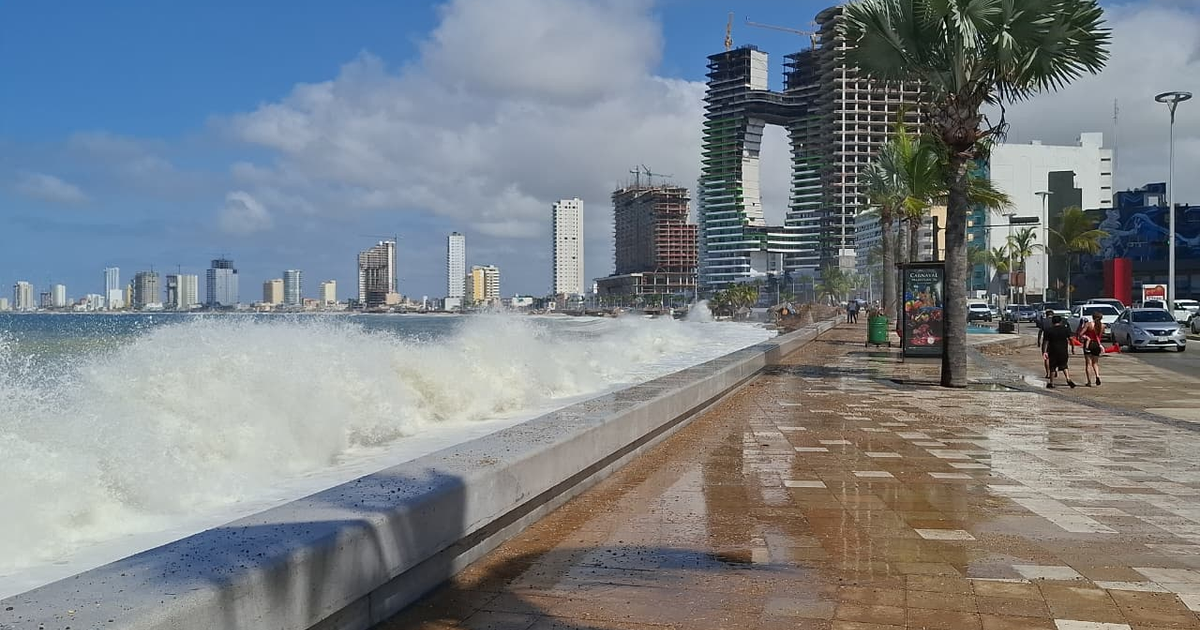 Olas rompiendo en el malecón de Mazatlán con edificios y palmeras al fondo
