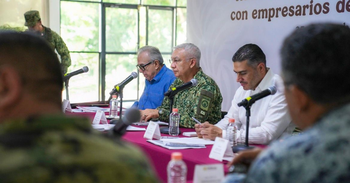 Personas en reunión de seguridad en Mazatlán, con micrófonos y documentos sobre la mesa.