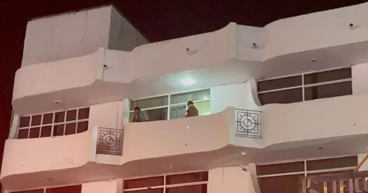 Edificio moderno con balcones en Mazatlán, iluminado de noche, con dos personas en un balcón superior.