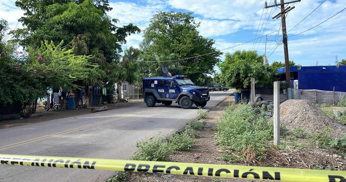 Vehículo blindado de la policía estatal en escena de crimen en Navolato, Sinaloa, con cinta de precaución y vegetación alrededor.