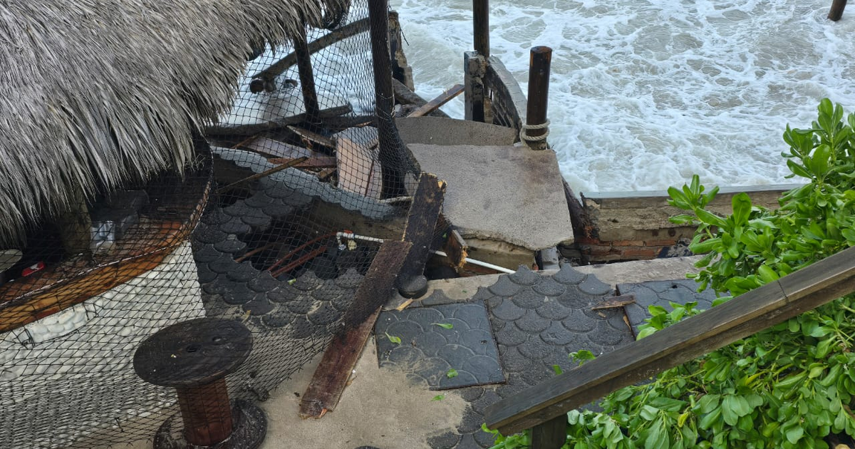 Estructura de madera dañada por oleaje en Mazatlán, con camino colapsado y olas visibles.