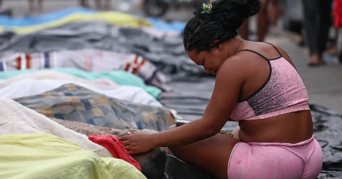 Mujer sentada en el suelo con mantas en un entorno urbano, sugiriendo situación de calle.