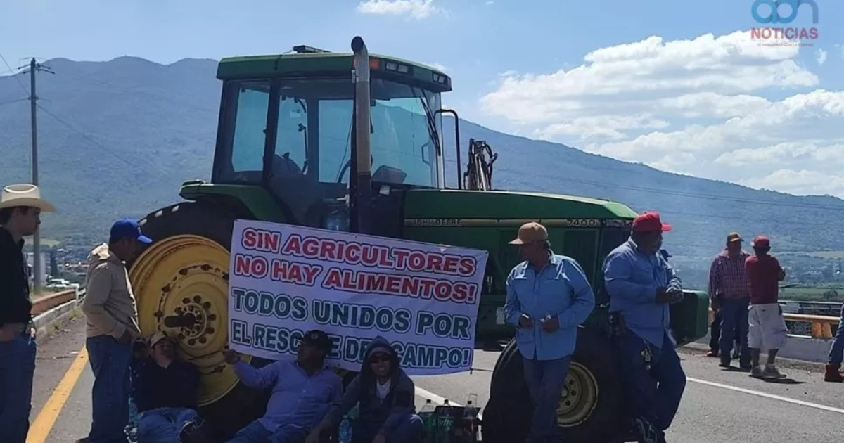Agricultores manifestándose cerca de un tractor con un cartel que dice 'SIN AGRICULTORES NO HAY ALIMENTOS'.
