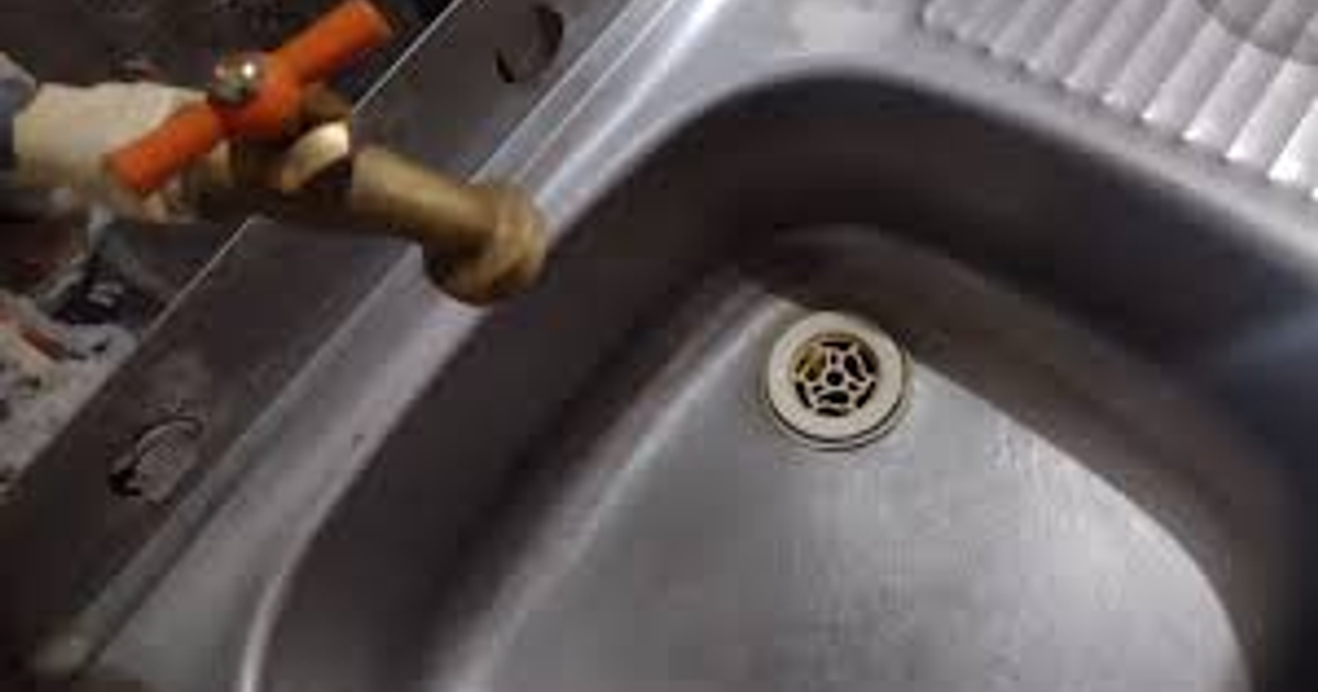 Fregadero de acero inoxidable con grifo de bronce y desagüe visible