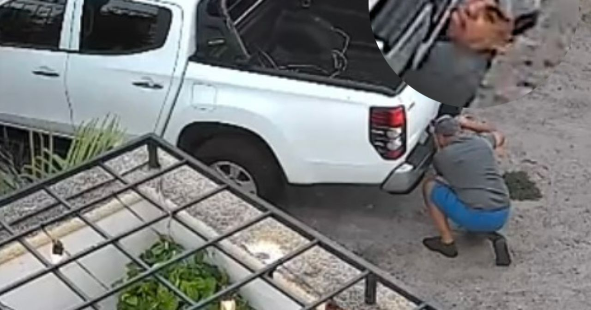 Hombre agachado junto a camioneta blanca en Mazatlán, captado por cámaras de seguridad durante robo de llanta de refacción.