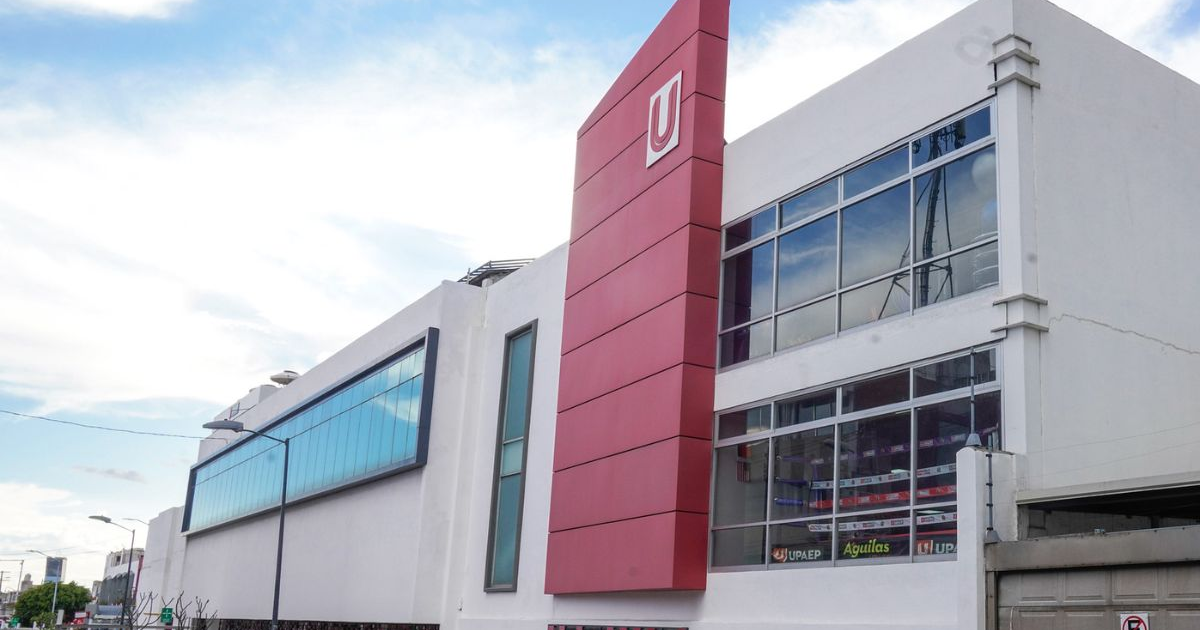 Edificio moderno de la UPAEP con fachada blanca y elemento rojo, cielo azul con nubes.