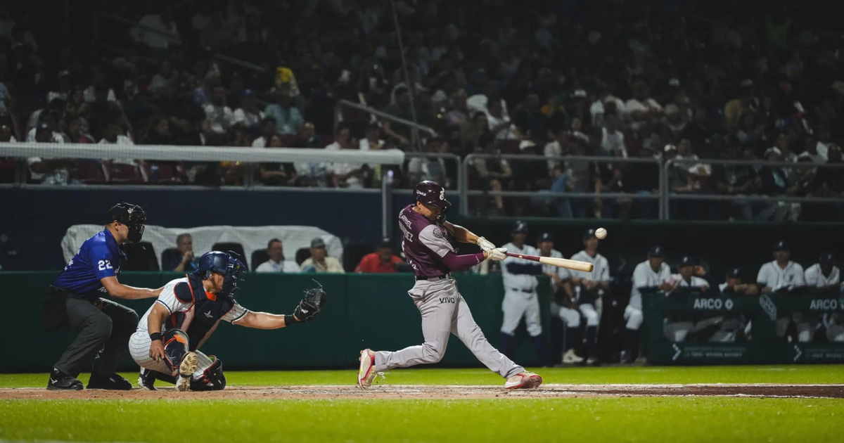 Jugador de béisbol bateando en un juego nocturno entre Venados de Mazatlán y Tomateros de Culiacán, con el receptor y el árbitro en posición.