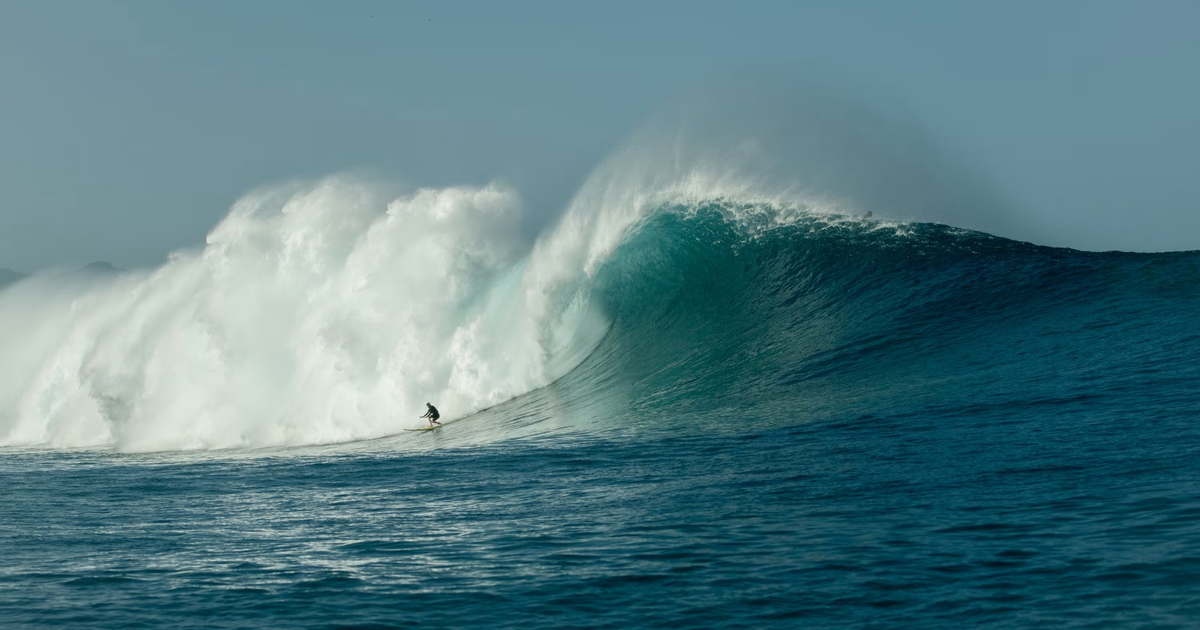 Surfista montando una gran ola azul con espuma blanca en Sinaloa durante la tormenta tropical Raymond.