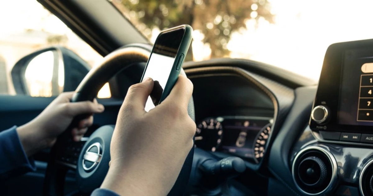 Persona conduciendo un automóvil mientras sostiene un teléfono móvil, destacando la distracción al volante.