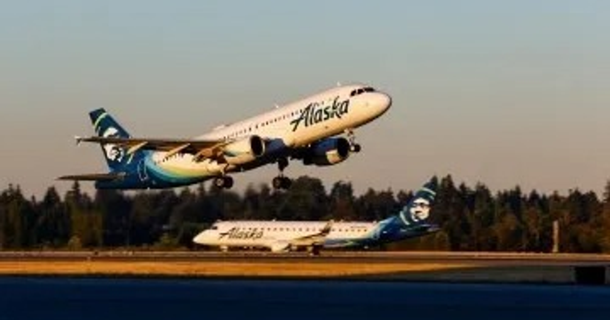 Dos aviones de Alaska Airlines en el Aeropuerto Internacional Rafael Buelna, uno despegando y otro en la pista, con un cielo despejado y árboles alrededor.