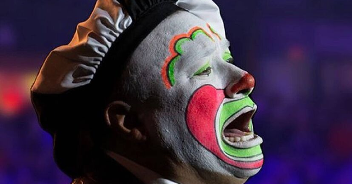 Payaso con maquillaje colorido y sombrero blanco y negro en un escenario de espectáculo.