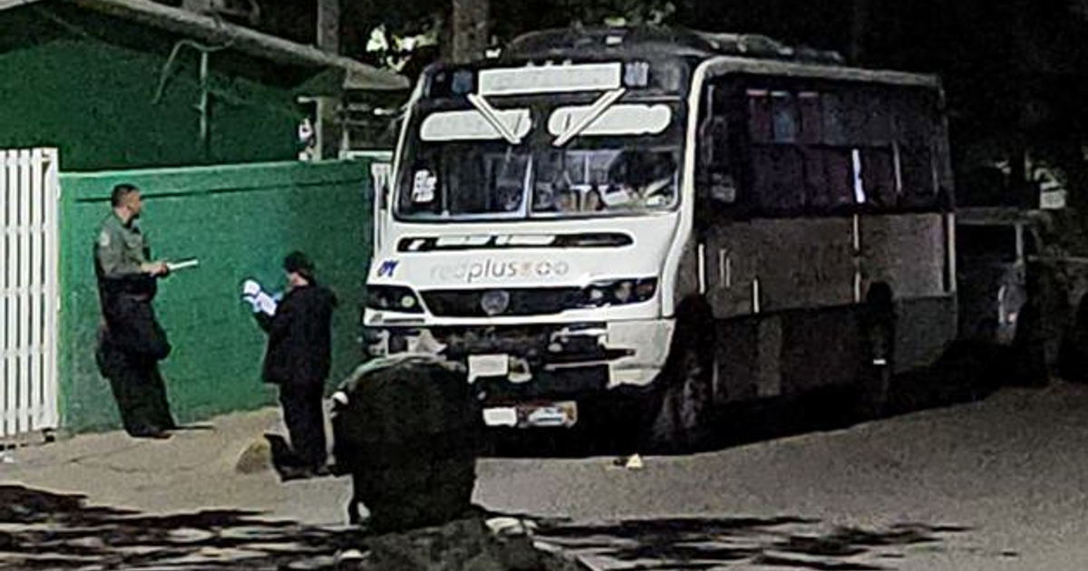 Autobús de la ruta CUCAS-Centro estacionado de noche en Culiacán con dos personas y un vehículo gris cercano.