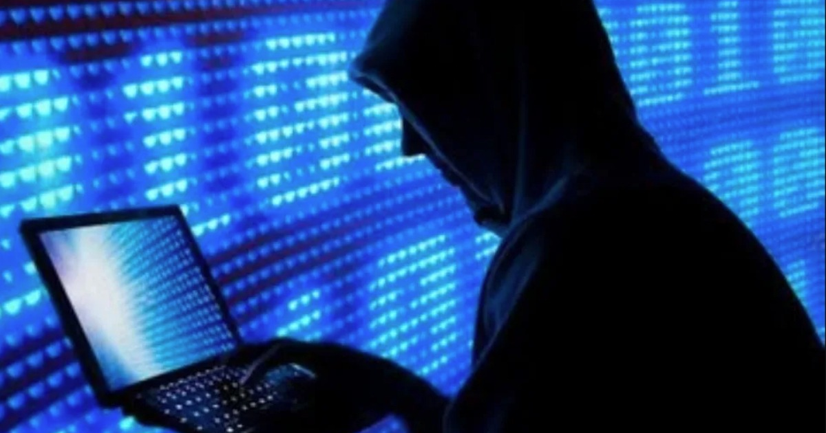 Silueta de hacker con capucha usando laptop, fondo azul pixelado, ciberseguridad.