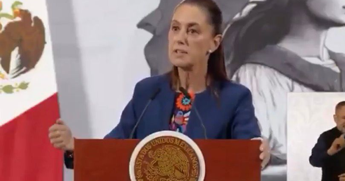 Claudia Sheinbaum hablando en un podio con intérprete de lengua de señas, bandera de México y emblema nacional de fondo.
