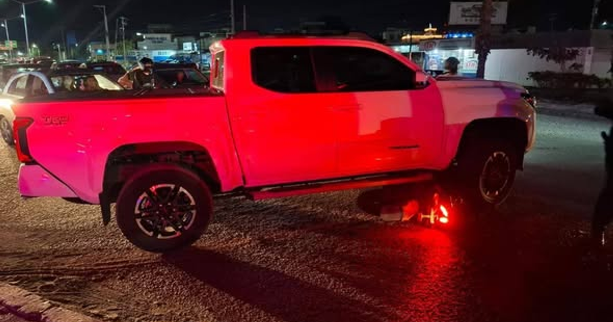 Camioneta blanca estacionada en calle de Mazatlán con luces rojas reflejadas, posible escena tras intento de asalto.