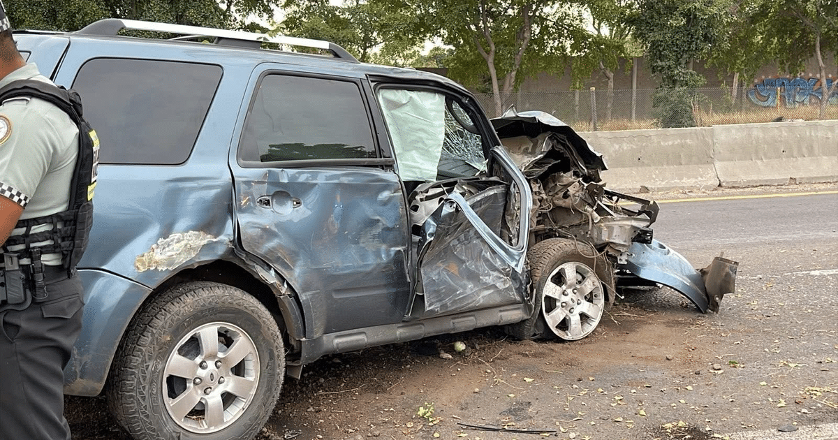 Un SUV azul dañado tras chocar contra un árbol en la Costerita, con un policía investigando el lugar