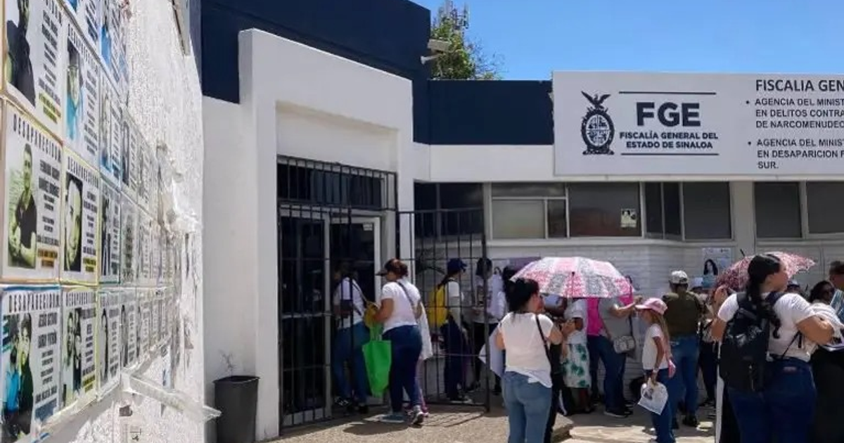 Fachada de la Fiscalía General del Estado de Sinaloa con carteles de personas desaparecidas y personas esperando en la entrada.