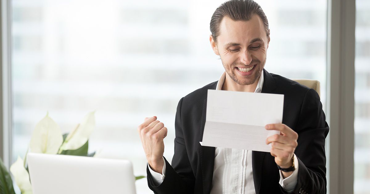 Hombre sonriente con carta y computadora, rodeado de plantas, simbolizando buenas noticias fiscales.