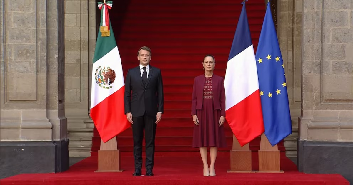 Claudia Sheinbaum y Emmanuel Macron en ceremonia oficial en Palacio Nacional con banderas de México, Francia y la UE.