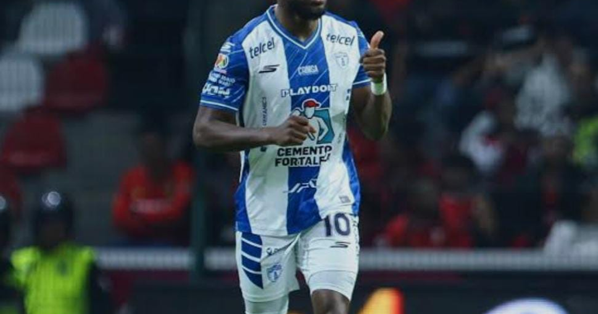 Jugador de fútbol en uniforme blanco y azul celebrando con pulgar arriba en un estadio.