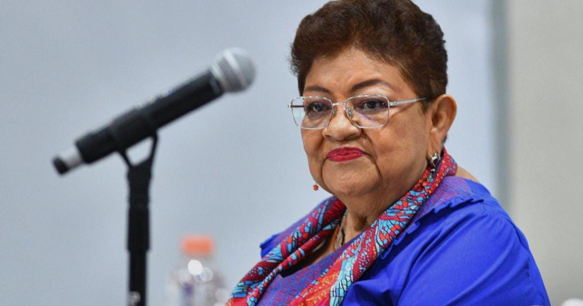 Posible imagen de Ernestina Godoy enfrente de un micrófono con atuendo colorido en conferencia.