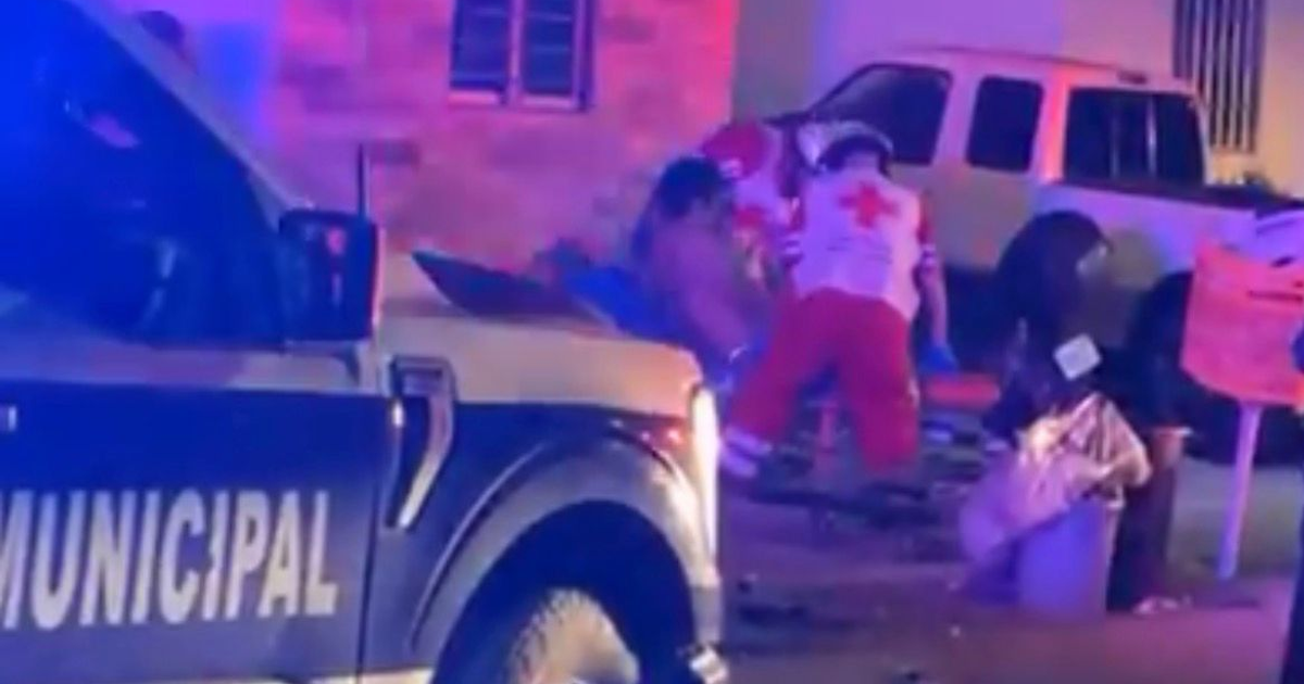 Paramédicos atienden a un herido de bala en Culiacán durante la noche, con una ambulancia iluminada en el fondo.