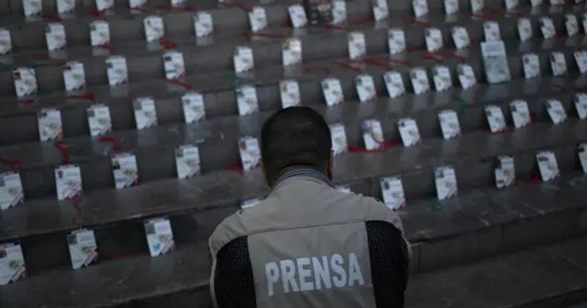 Periodista con chaleco 'PRENSA' frente a carteles conmemorativos en escaleras, simbolizando la lucha contra la impunidad en México.