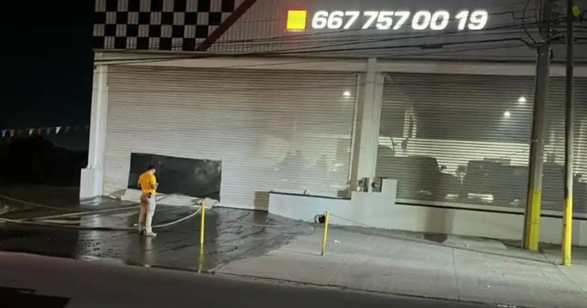 Hombre observando área exterior del lote Elite Motors Sport en Culiacán después de incendio nocturno de vehículos.