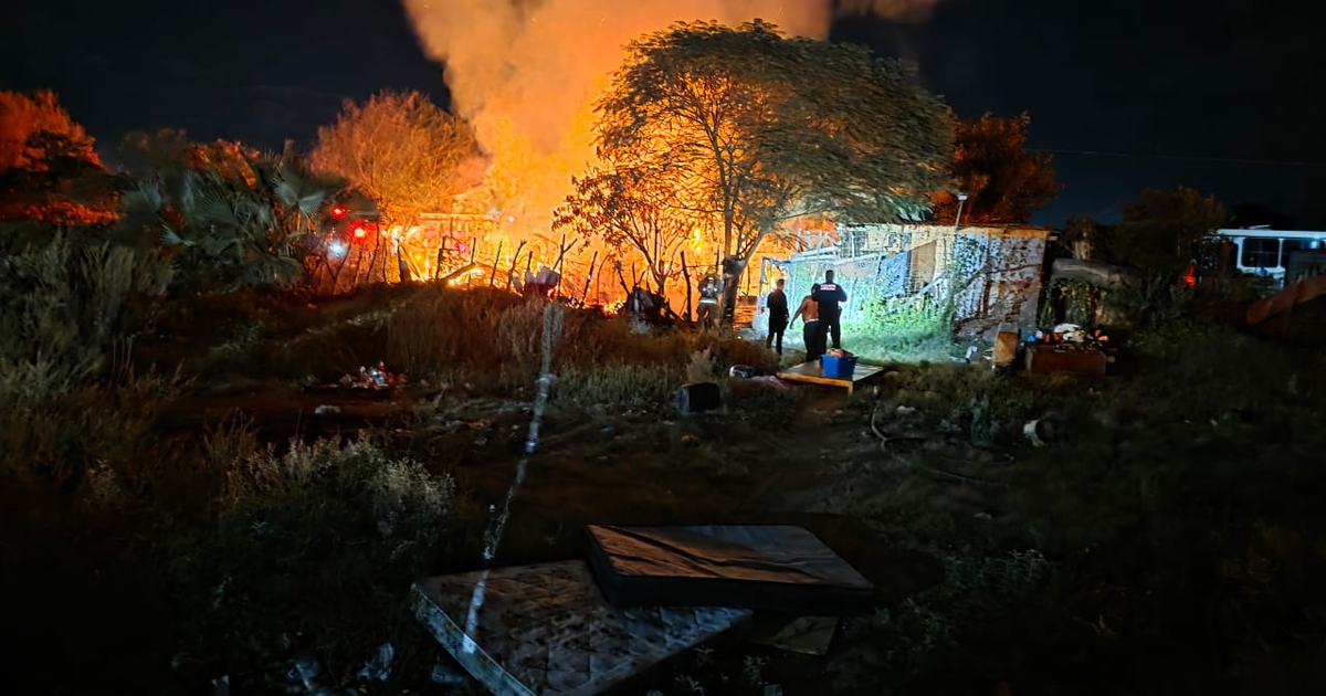 Incendio nocturno en Los Mochis con llamas y humo, personas y servicios de emergencia presentes.