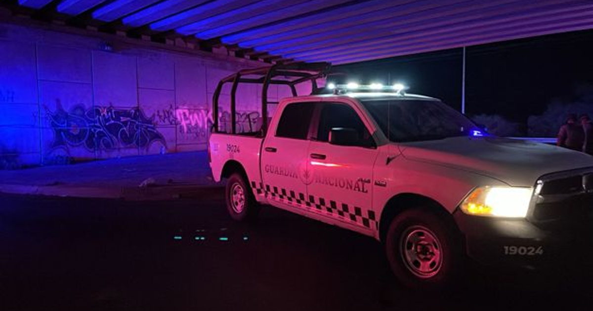 Vehículo de la Guardia Nacional bajo un puente en Culiacán, iluminado por luces de emergencia y rodeado de grafitis.