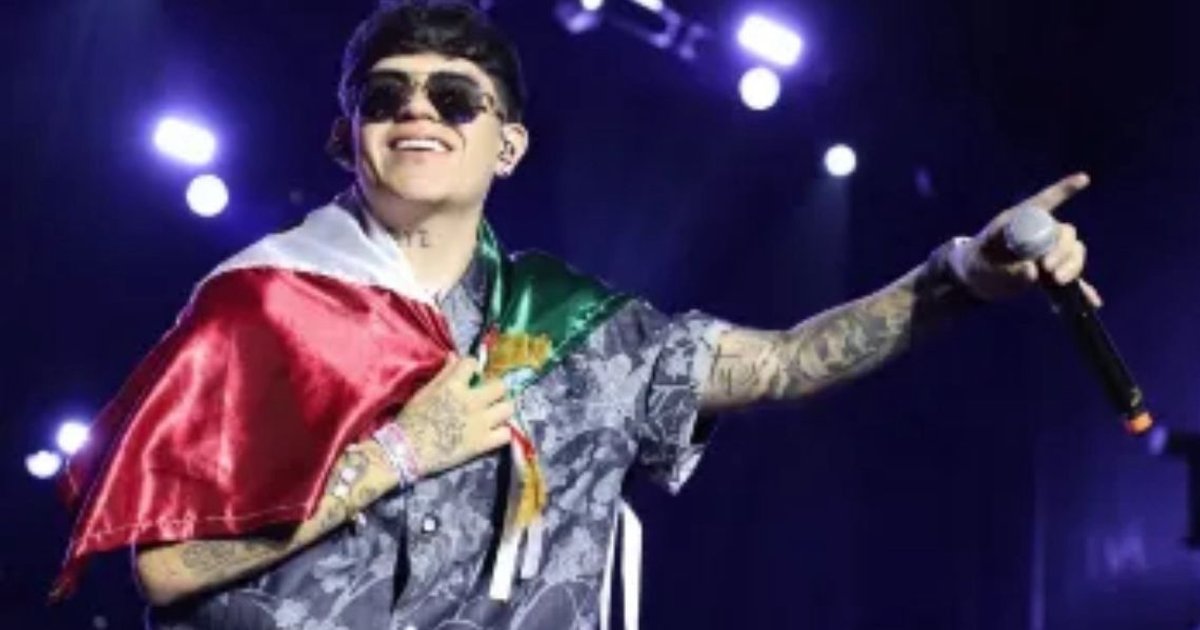 Junior H en el escenario con bandera mexicana y micrófono