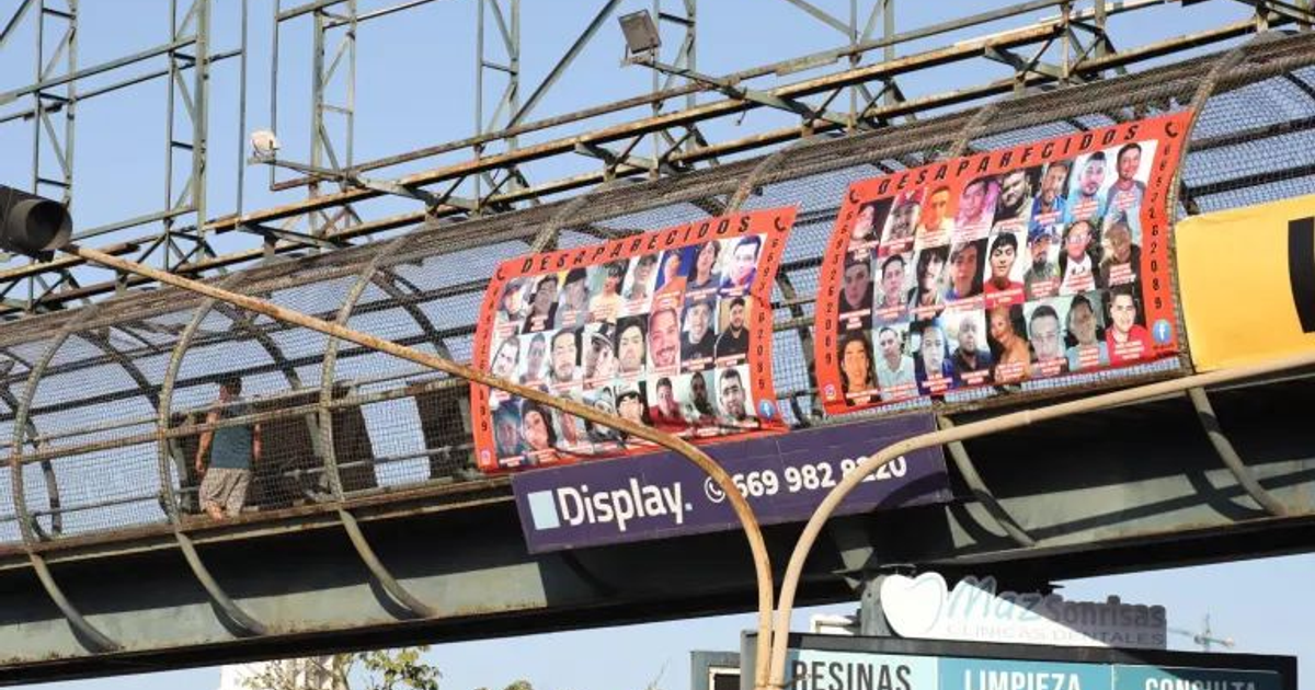 Puente peatonal en Mazatlán con carteles de personas desaparecidas y un hombre caminando.